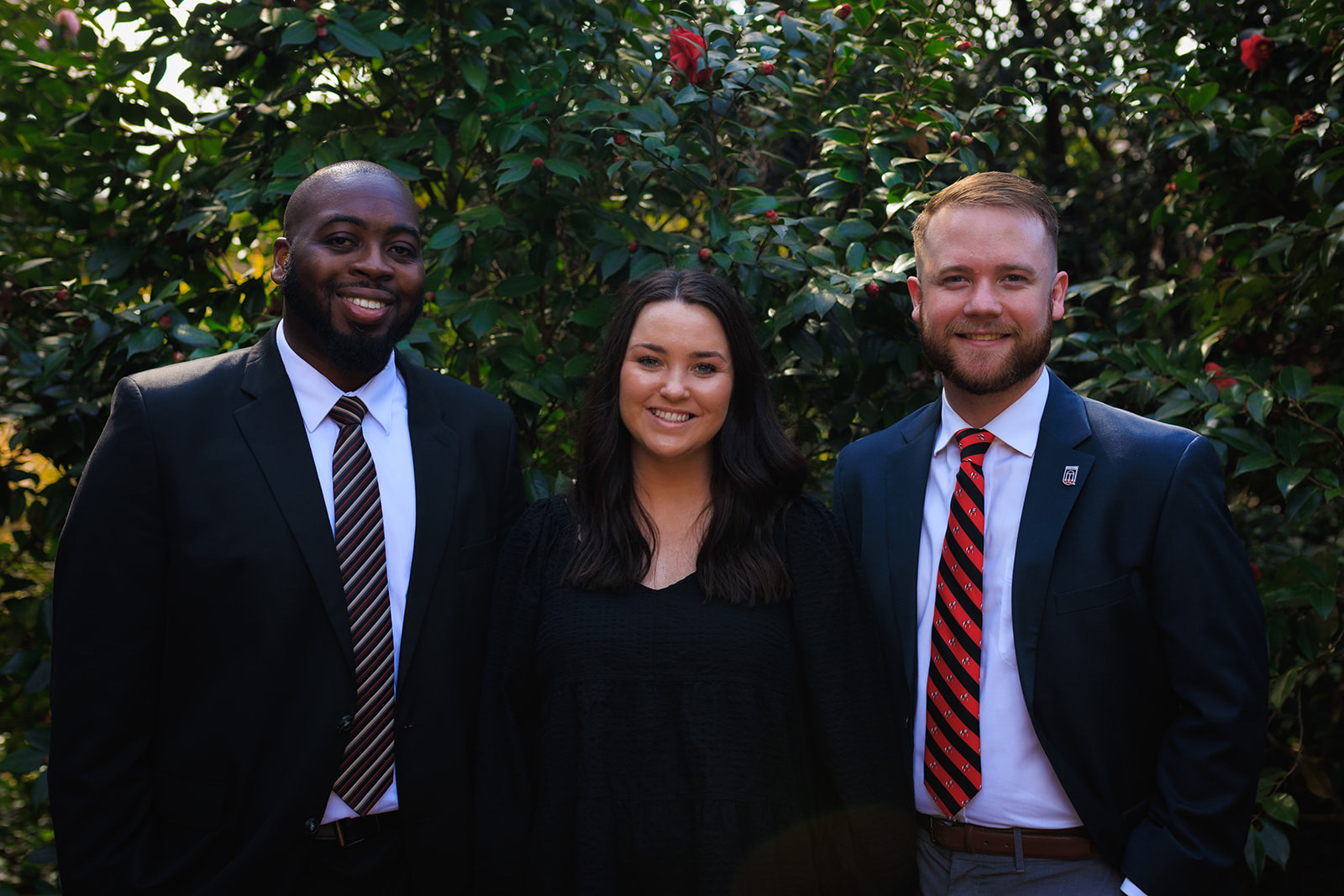 Three Greek Life Assistant Directors standing together with trees behind them.