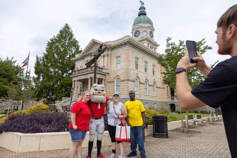 Three people with hairy dawg getting their photo taken outside of a UGA building.